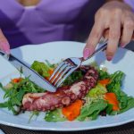 Woman enjoying an octopus salad with fresh greens outdoors. Vibrant and appetizing.